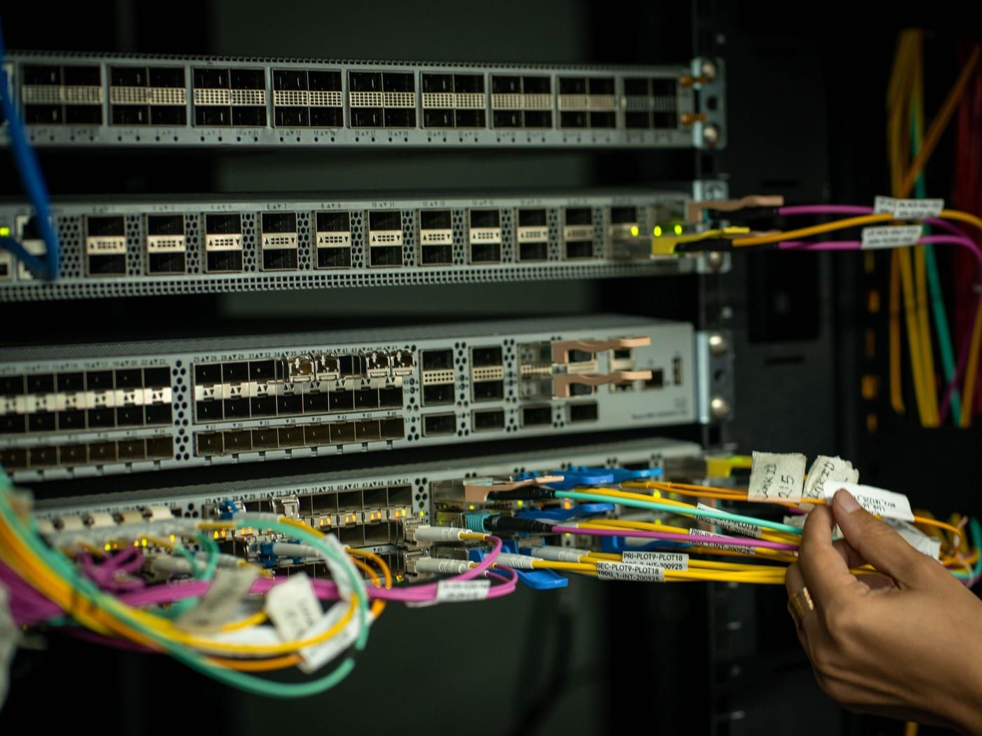 Eine Hand steckt beschriftete Netzwerkkabel in einem dunklen Serverschrank um